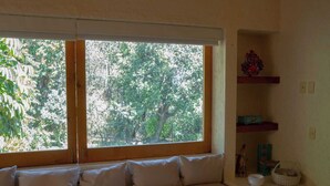 A room with a large window, a sofa with cushions, and a shelf with decorative items. - Zapote House (Malinalco)