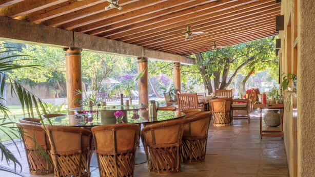 An outdoor patio with a round table and wicker chairs, surrounded by large wooden pillars and a tiled floor. - Zapote House (Malinalco)