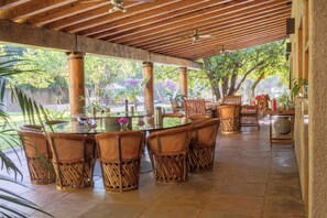 Eine Terrassengaststätte mit einem runden Tisch und Korbstühlen, umgeben von hohen Holzsäulen und einem gefliesten Boden.