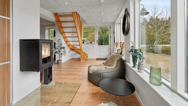 A modern living room with a fireplace, a wooden staircase, and large windows. - Modern house with space for relaxation (Aakirkeby)