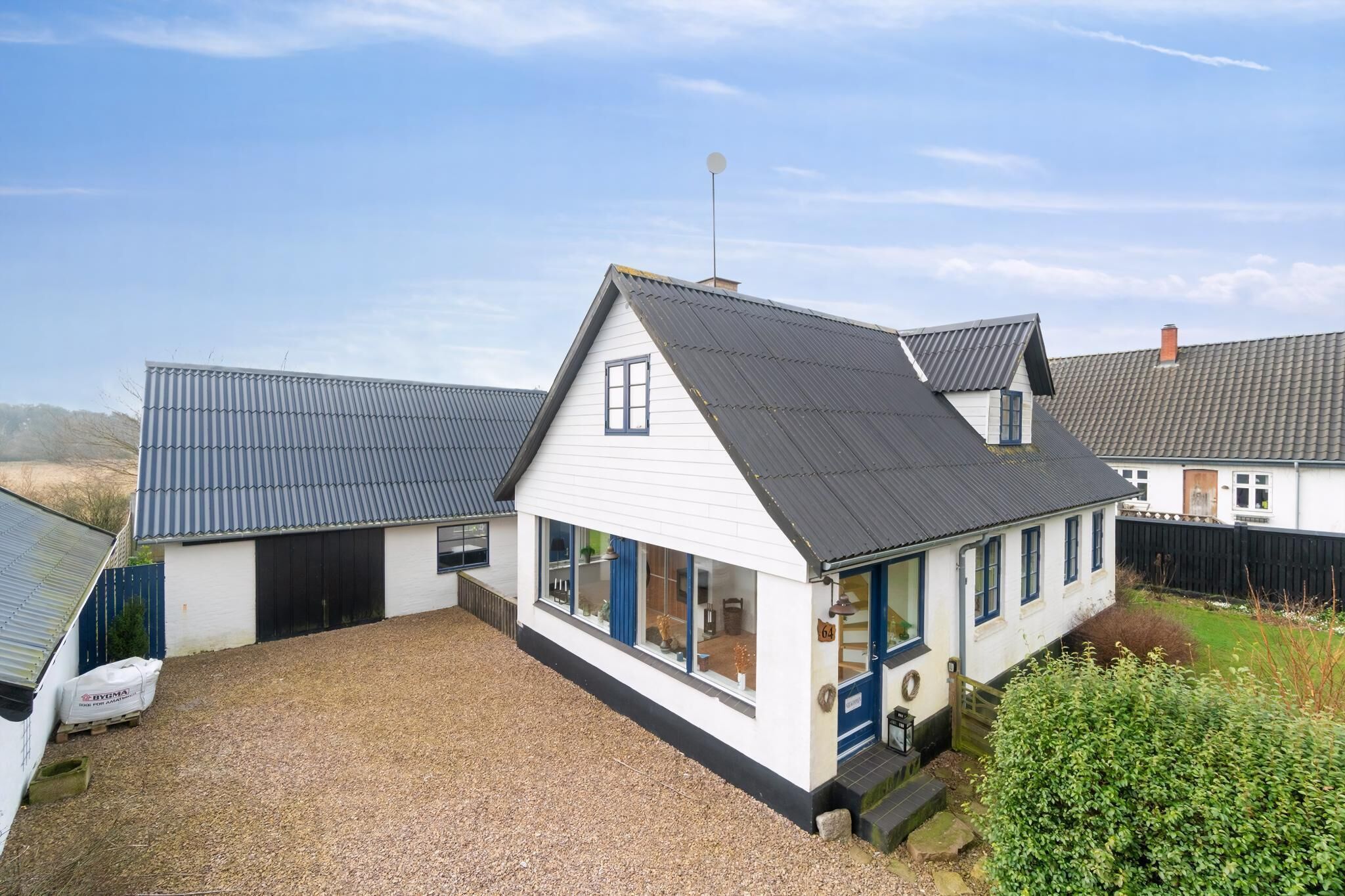 A white building with a dark roof, a garage, and a gravel driveway.