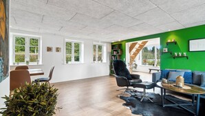A spacious room with a wooden floor, a black leather chair, a sofa, a coffee table, and a green accent wall. - Modern house with space for relaxation (Aakirkeby)