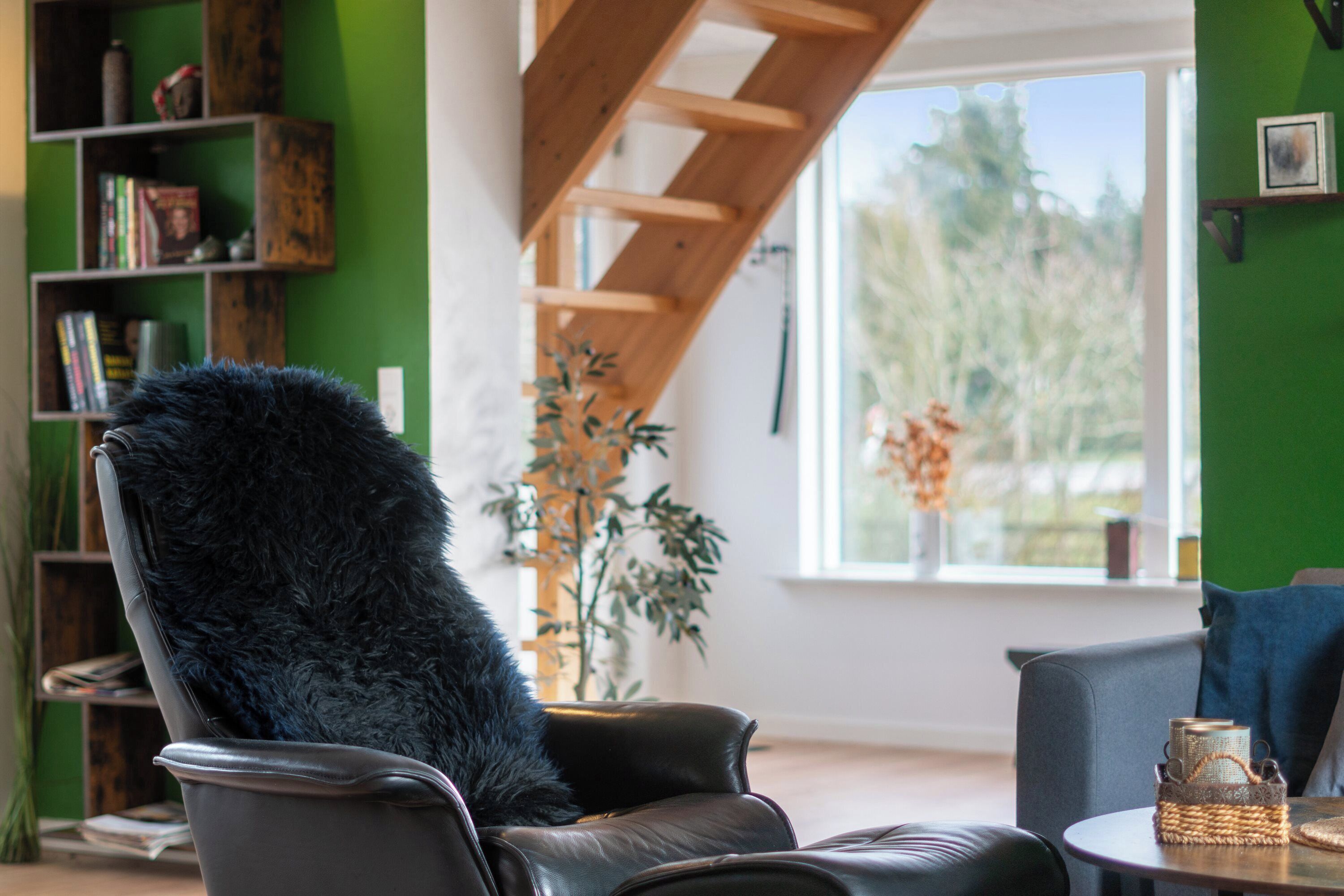 Une pièce comprenant un fauteuil en cuir noir, une bibliothèque en bois, une fenêtre donnant sur des arbres et une table sur laquelle se trouve un panier en osier.