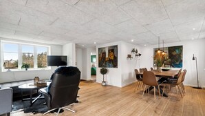 A spacious room with a dining area, a large window, and artwork on the walls. - Modern house with space for relaxation (Aakirkeby)