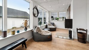 A modern living room with large windows, a fireplace, and a TV. - Modern house with space for relaxation (Aakirkeby)