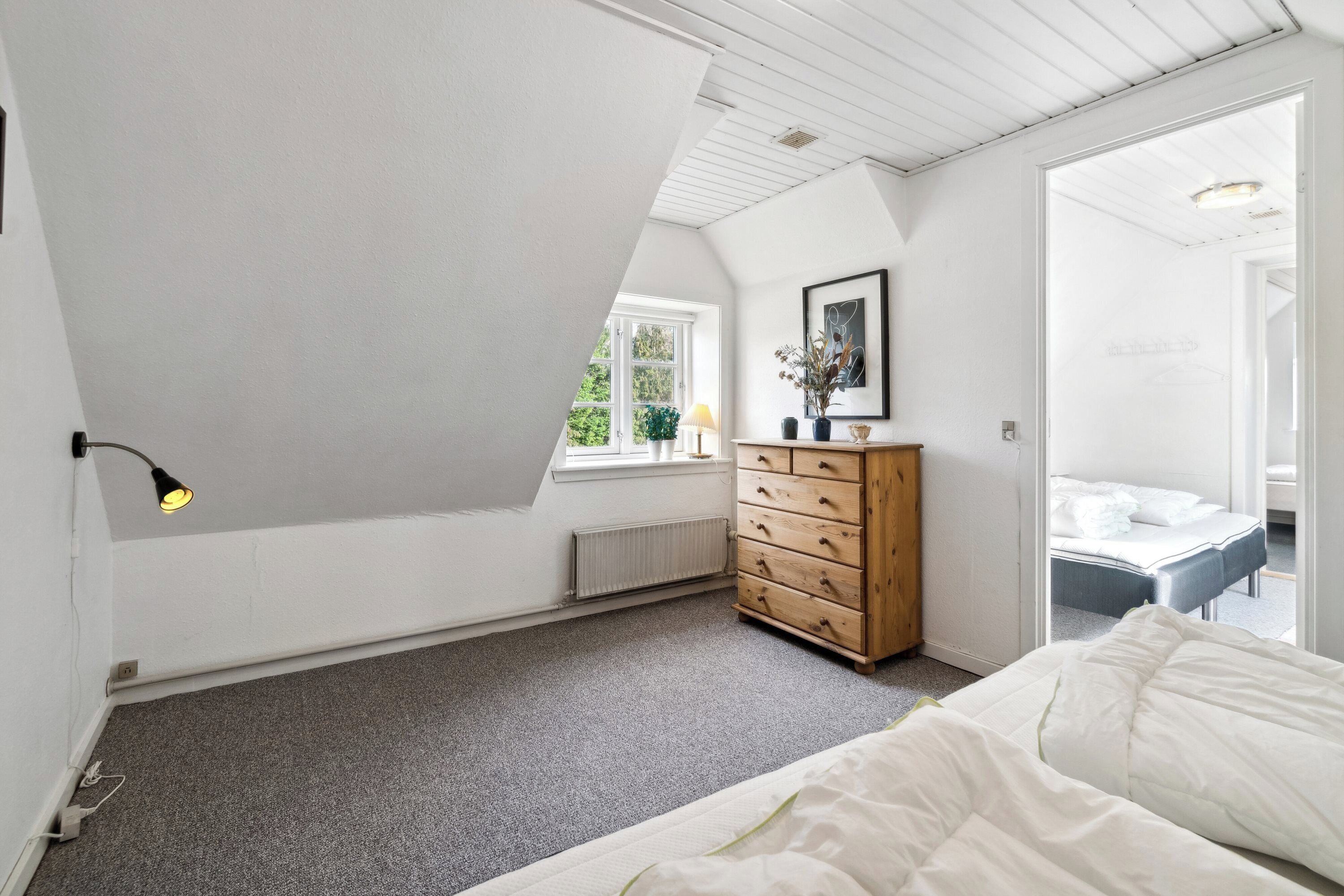 Un dormitorio con techo inclinado, un aparador de madera, una cama y una ventana con vistas a la vegetación.