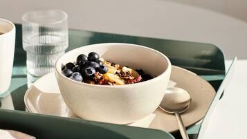 A bowl of cereal with blueberries and granola on a white plate, a glass of water, and a spoon on a green tray.