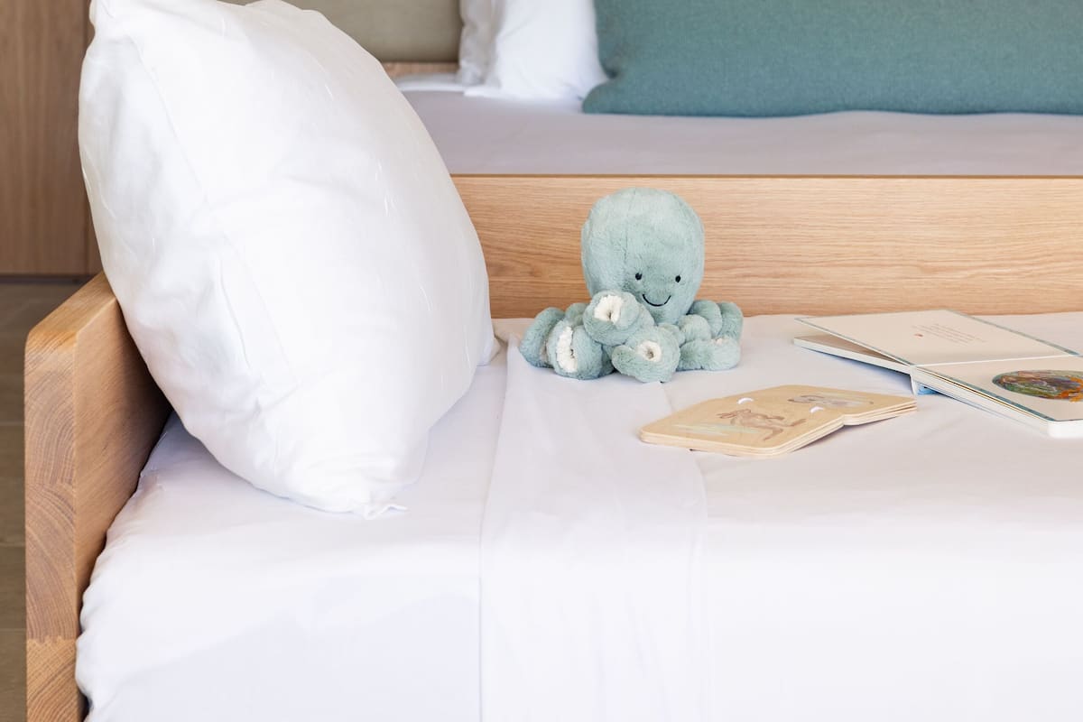 A bedroom with a bed, pillows, a stuffed toy, and a book.