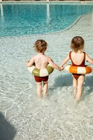 Dos niños con flotadores caminando hacia una piscina.
