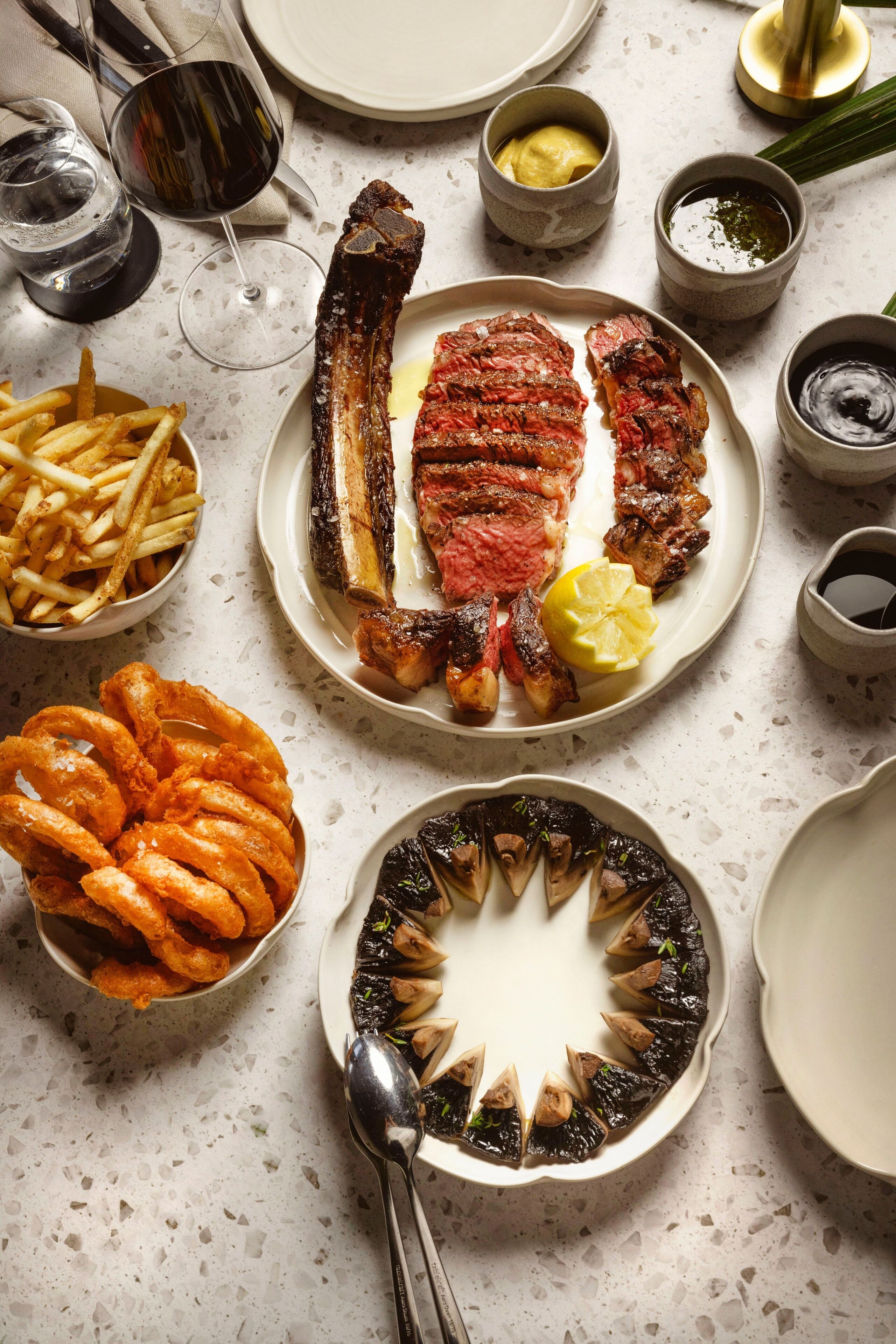 A dining table with various dishes including steak, fries, onion rings, and grilled vegetables.