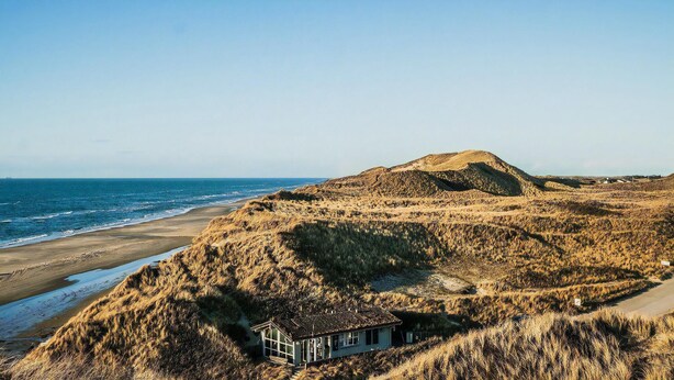 A coastal landscape with a dune, a beach, and a house with a sloped roof. - Unique location on a large sunny natural plot (Ålbæk)