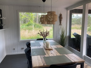 Un comedor con una mesa de madera, sillas negras, un jarrón con flores secas y vistas al exterior.