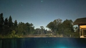 A nighttime view of a swimming pool with two illuminated lights, surrounded by trees and a building. - Unique location on a large sunny natural plot (Ålbæk)