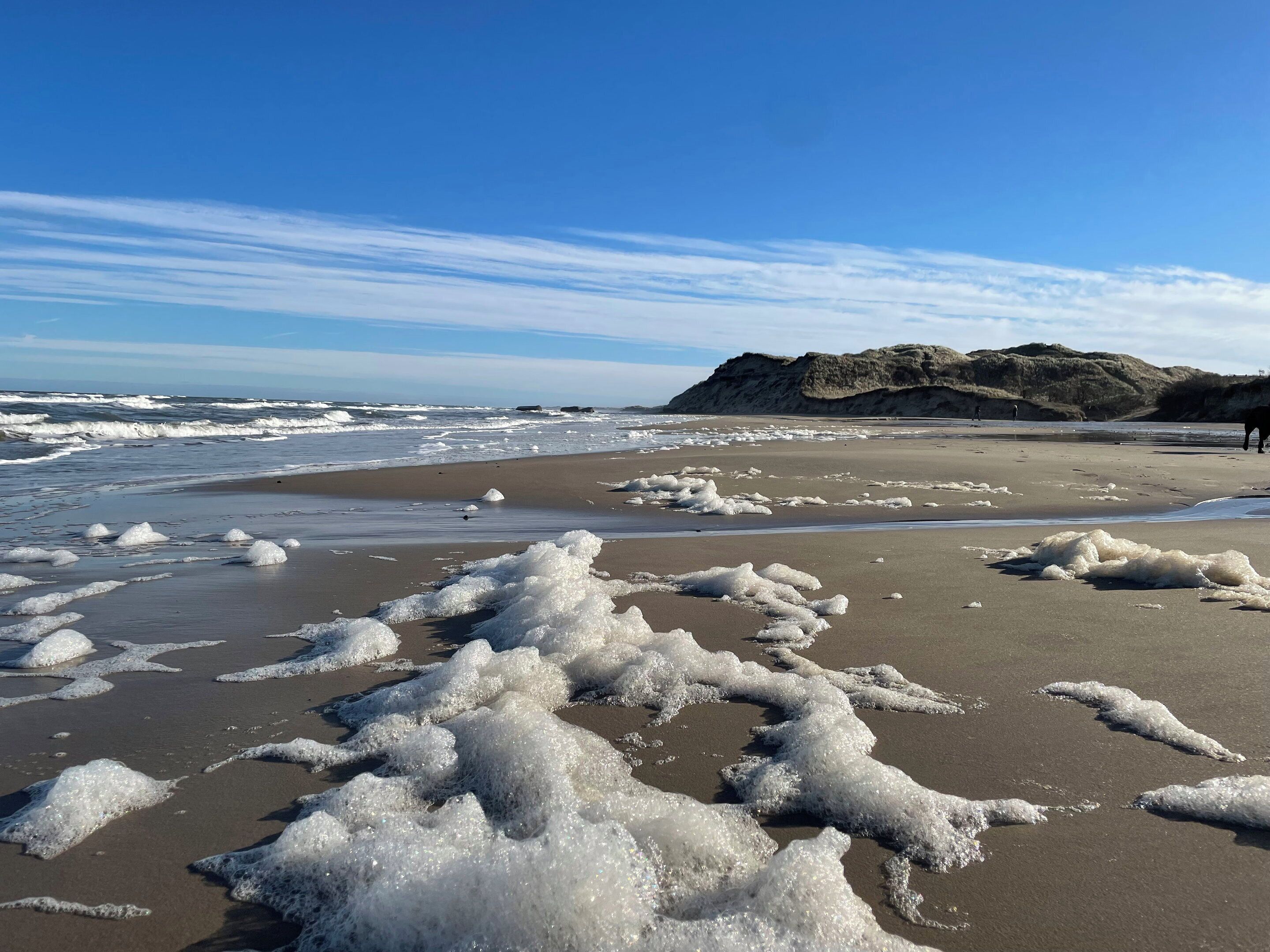 A beach with waves, sand, and a distant hill.