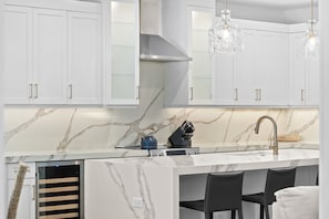 Cozinha moderna com armários brancos, painel de fundo em mármore e ilha planejada com pia e bancada.