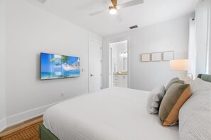 Quarto com cama grande, ventilador de teto, TV fixada na parede e vista para o banheiro.