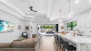 A modern kitchen with a marble countertop, a bar area, and a view of the outdoor pool area. - LUXE: Home w/ 3 Kings, Pool & Spa, Bikes, BBQ (Naples)