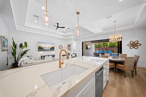 A modern kitchen with a large island, pendant lighting, and a dining area with wicker chairs. - LUXE: Home w/ 3 Kings, Pool & Spa, Bikes, BBQ (Naples)