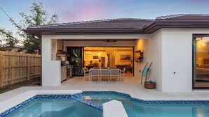 A modern house with a swimming pool, a patio with outdoor furniture, and a visible kitchen area. - LUXE: Home w/ 3 Kings, Pool & Spa, Bikes, BBQ (Naples)
