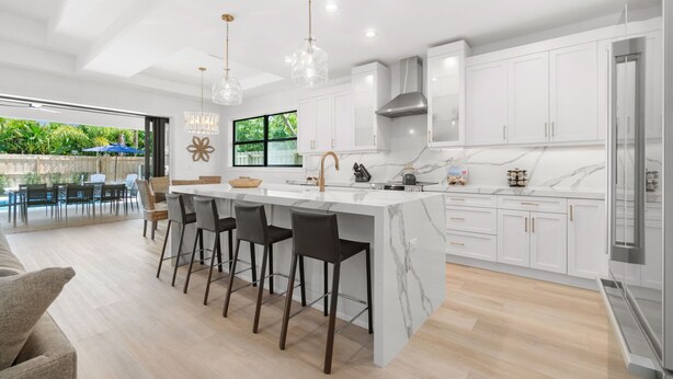 A modern kitchen with a marble countertop, white cabinets, and a central island with bar stools. - LUXE: Home w/ 3 Kings, Pool & Spa, Bikes, BBQ (Naples)