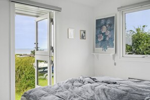 A bedroom with a bed, an open door to a garden, and a window with a view of greenery.