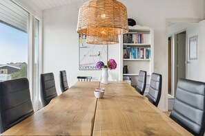 A conference room with a wooden table, black chairs, a white vase with flowers, and a bookshelf with books.