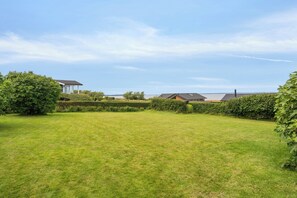 A spacious lawn with a clear sky, surrounded by well-maintained hedges and a few buildings in the background.
