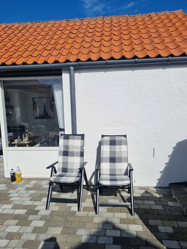 A patio with two chairs, a window, and a tiled roof.