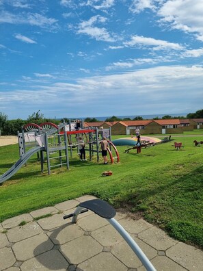A playground with a slide and climbing structures, surrounded by green grass and a clear sky. - Lovely holiday home in Allinge for 6 guests (Allinge)