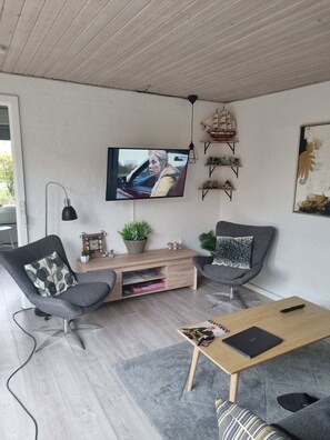 A modern living room with a TV, two grey armchairs, a wooden coffee table, and a small TV stand with decorative items. - Lovely holiday home in Allinge for 6 guests (Allinge)
