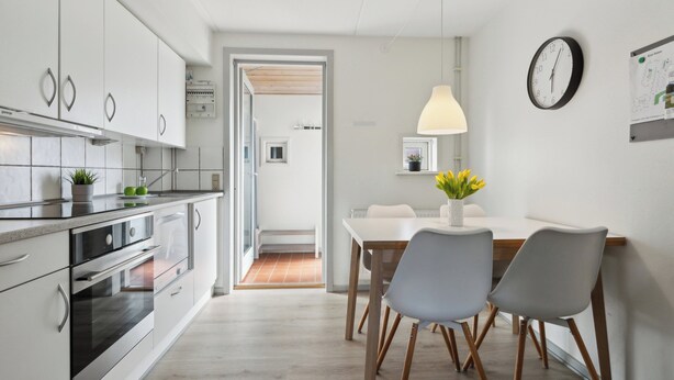 A modern kitchen with white cabinets, stainless steel appliances, and a dining area with a white table and chairs. - Summer house on beautiful Rømø! (Rømø)