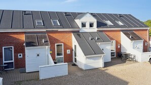 A row of white mobile homes with grey roofs, a gravel driveway, and a small patio area with outdoor seating. - Summer house on beautiful Rømø! (Rømø)