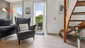 A modern living room with a sofa, armchair, wooden staircase, and a view through a glass door. - Summer house on beautiful Rømø! (Rømø)