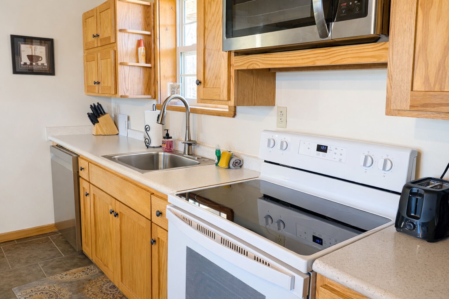 A kitchen with wooden cabinets, a stainless steel sink, a microwave, a stove, and a toaster.