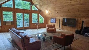 En rymlig loftvåning med stora fönster, en takfläkt, en lädersoffa, en röd fåtölj och en platt-TV.