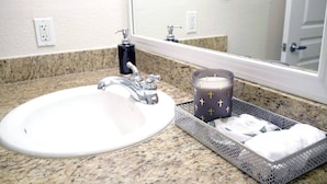 A bathroom sink with a granite countertop, a mirror, a faucet, a soap dispenser, and a candle holder with a candle.