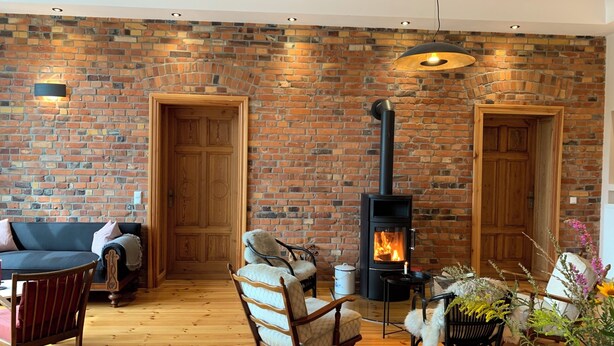 A cozy living room with a brick wall, wooden furniture, and a wood-burning stove. - Spacious double room surrounded by greenery (Vetschau/Spreewald)