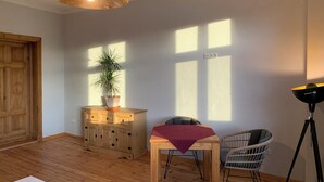 A room with a wooden floor, a table with a red tablecloth, two wicker chairs, a potted plant, a wooden cabinet, and a pendant light. - Spacious double room surrounded by greenery (Vetschau/Spreewald)
