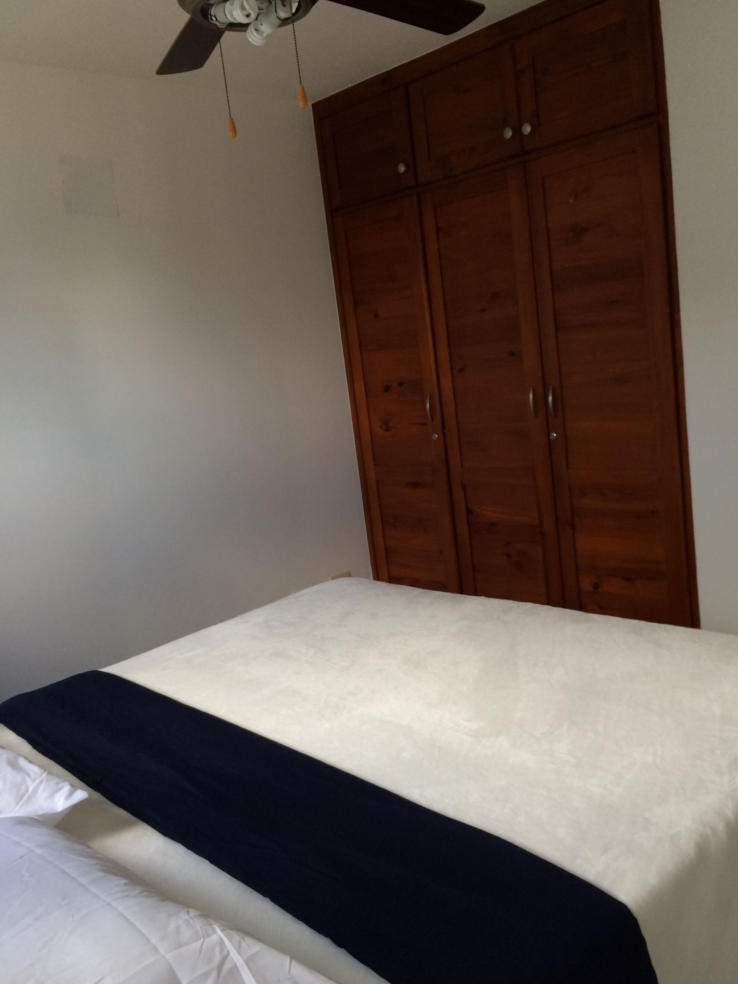 Ein Schlafzimmer mit einem Bett, einem Holzschrank und einem Deckenventilator.