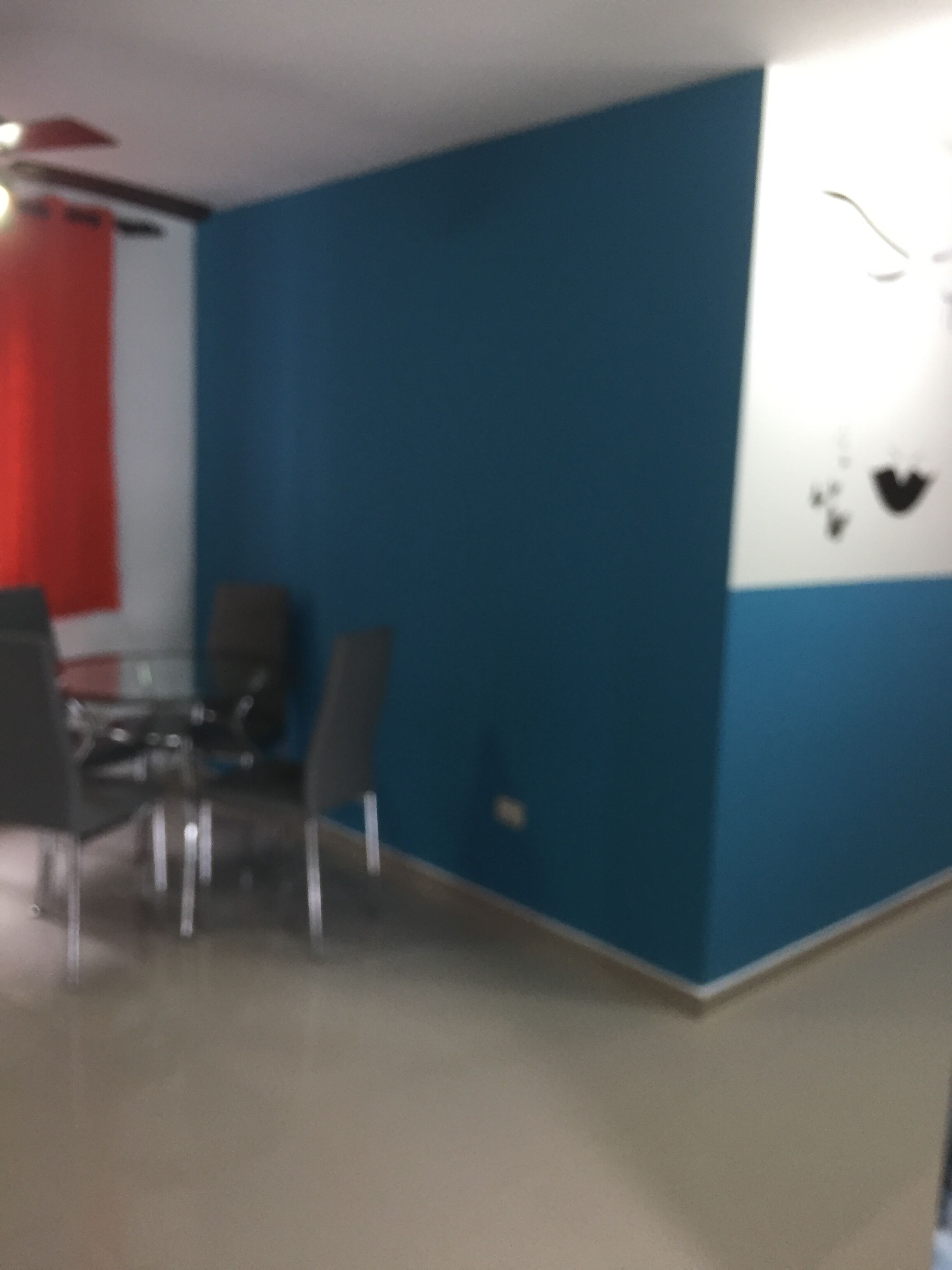 A room with a blue and white wall, a glass table with chairs, and a ceiling fan.