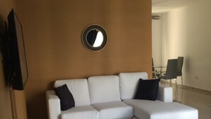 Una sala de estar moderna con un sofá seccional blanco, un espejo redondo en la pared y un ventilador de techo.