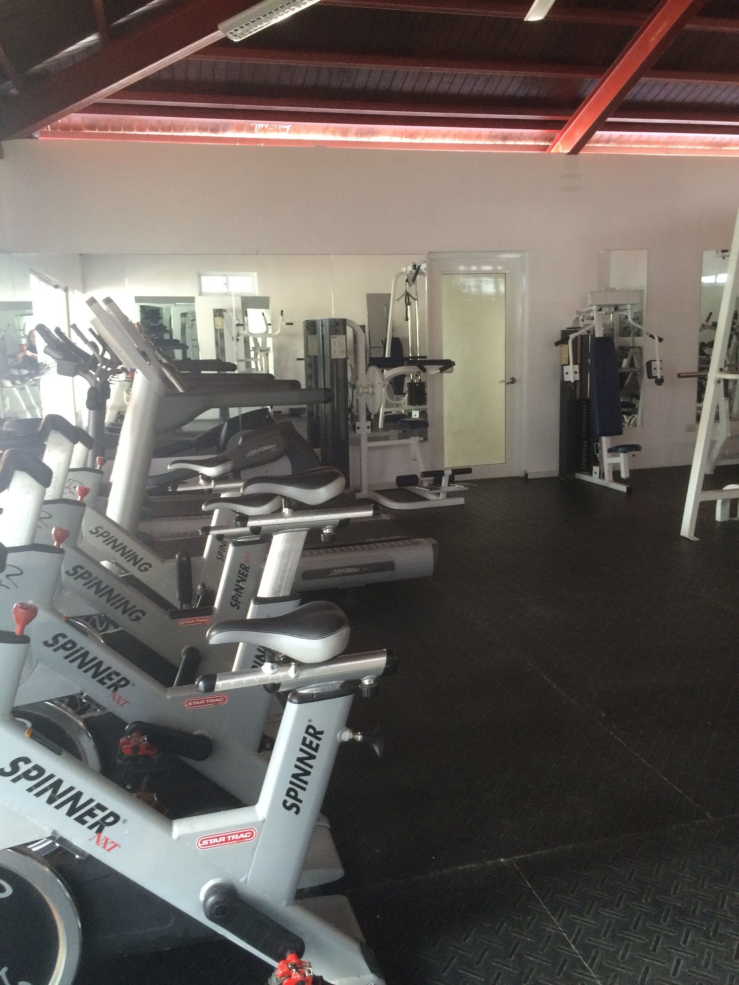 Une salle de sport équipée de plusieurs vélos de spinning, de machines de musculation et d’un mur recouvert de miroirs.