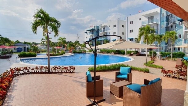 Un área de piscina con sillones de descanso y una palmera, rodeada de edificios.