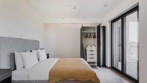 Un dormitorio moderno con cama, mesitas de noche, armario y un ventanal grande.