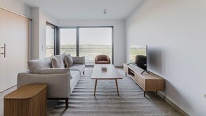 Una sala de estar moderna con sofá, sillón, mesa de centro, televisor y un ventanal con vistas al exterior.