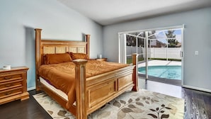 A bedroom with a wooden bed, a nightstand, a dresser, and a view of a swimming pool through a glass door. - Tampa Paradise For All Occasions (Riverview)