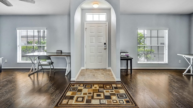 A spacious room with hardwood flooring, a white door, and two windows with blinds. - Tampa Paradise For All Occasions (Riverview)