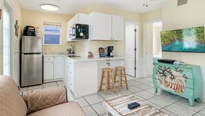 A compact kitchen with white cabinets, a stainless steel refrigerator, a microwave, and a coffee maker. There is a teal-colored dresser with a decorative design and a flat-screen TV mounted above it. - 50 Steps to Beach, Family Friendly, Heated Pool (Indian Rocks Beach)
