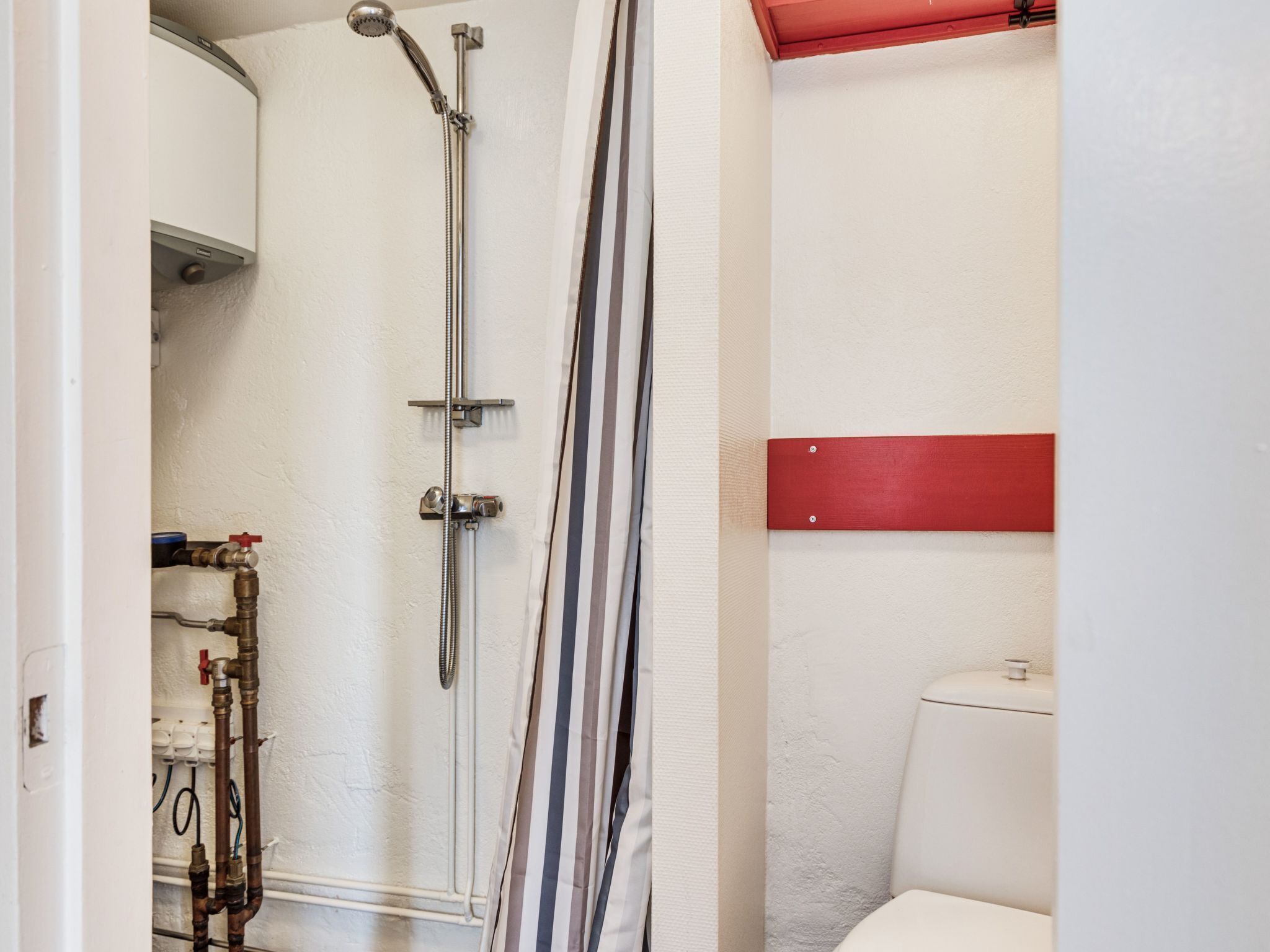 Een badkamer met een douche, toilet en zichtbare leidingen.