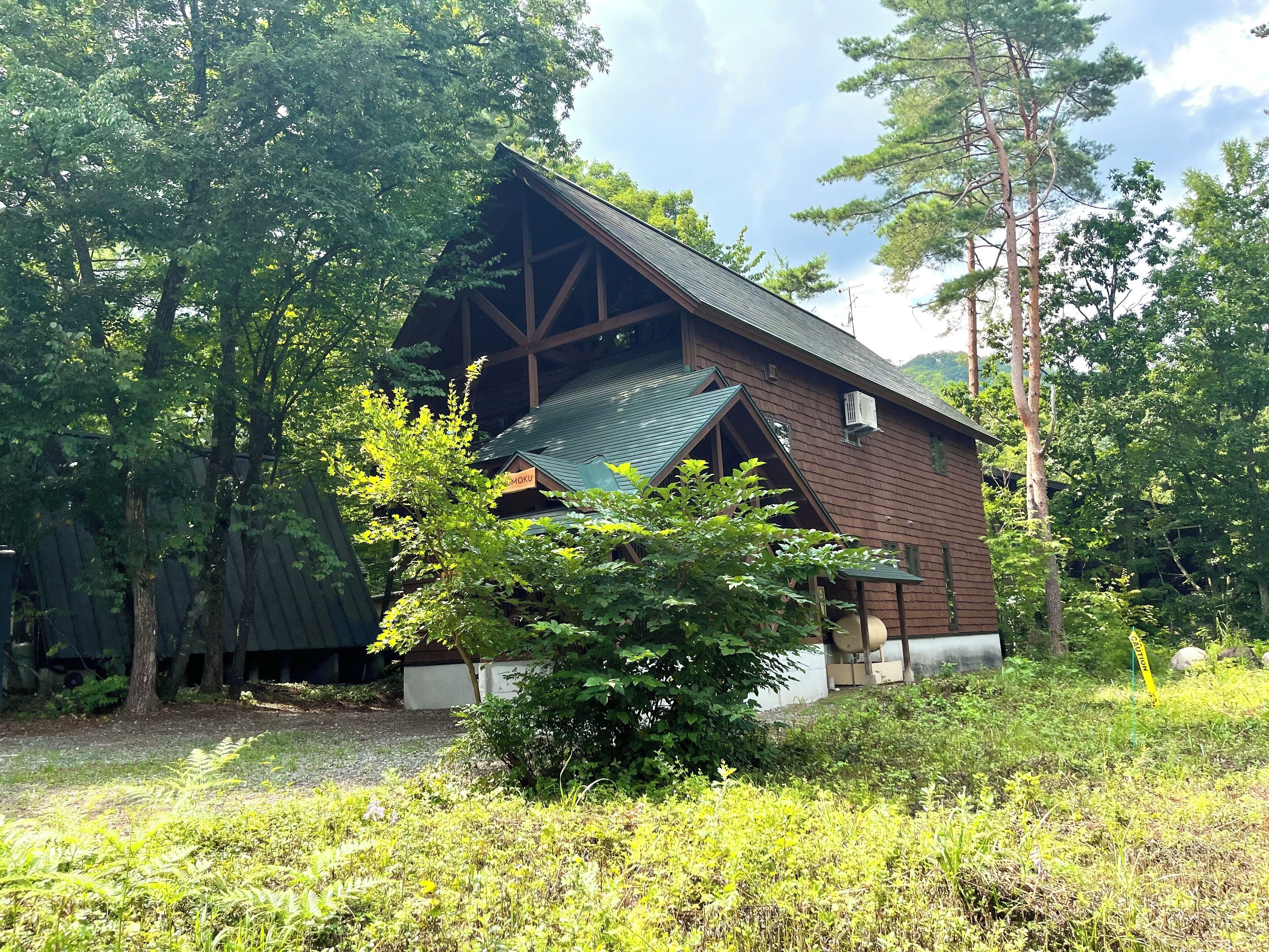 A rustic wooden cabin with a sloped roof, surrounded by dense trees and greenery.
